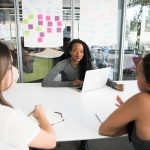 A diverse group of women collaborates around a desk in a modern office setting.