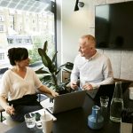 Two business professionals engaging in a team meeting in a modern London office with a large window view.