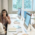 Diverse group of women working together in a modern office setting, fostering teamwork and creativity.