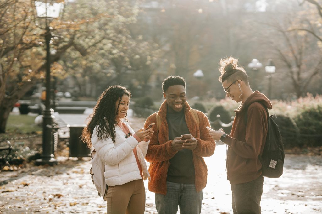 Three diverse young adults enjoying social media together in a sunny park.