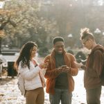 Three diverse young adults enjoying social media together in a sunny park.