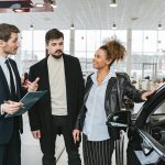 A diverse team of adults discussing a car purchase in a dealership showroom.