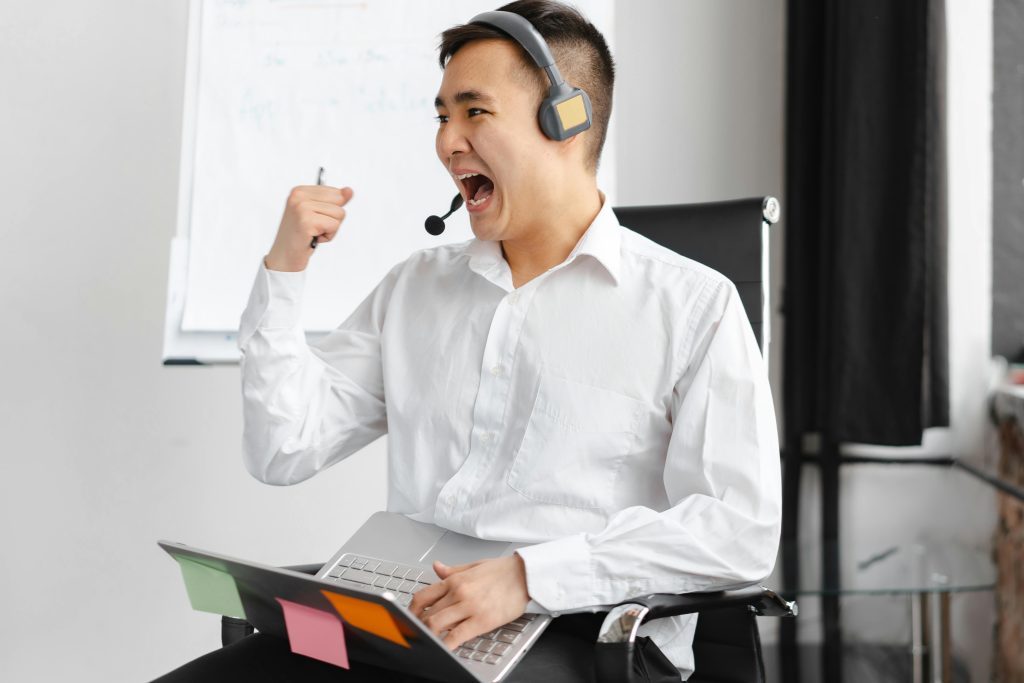 Asian call center agent in office celebrating a successful call with expressive gesture.