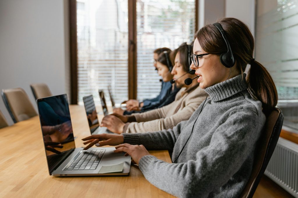 Professional customer service team working in a modern office setting with headsets and laptops.