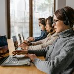 Professional customer service team working in a modern office setting with headsets and laptops.