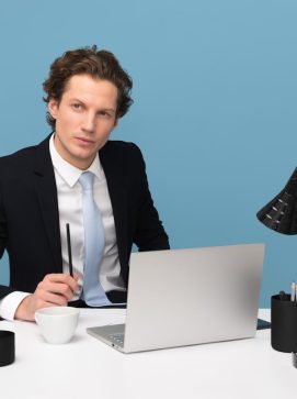 A focused businessman in a suit works at his tidy desk with a laptop, plant, and lamp.