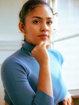 A serene and elegant portrait of a young woman in a blue turtleneck, captured indoors by a window.